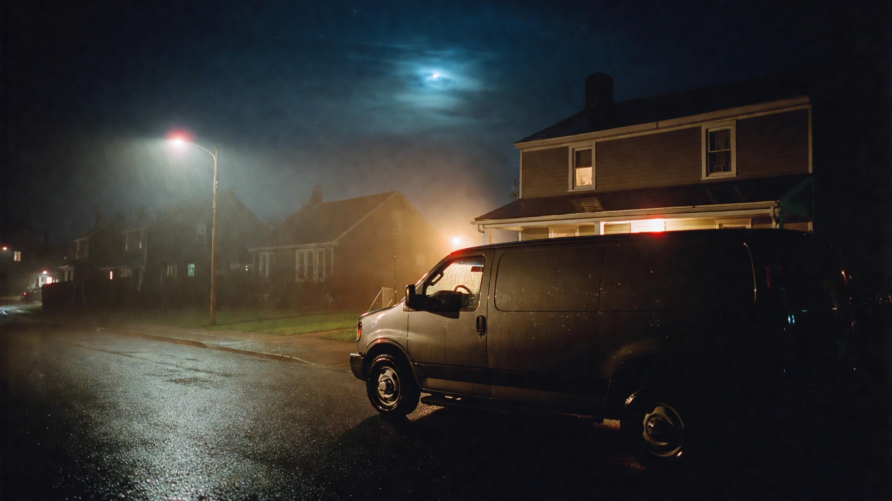 A trade van parked on a quiet suburban street at night, one porch light on.