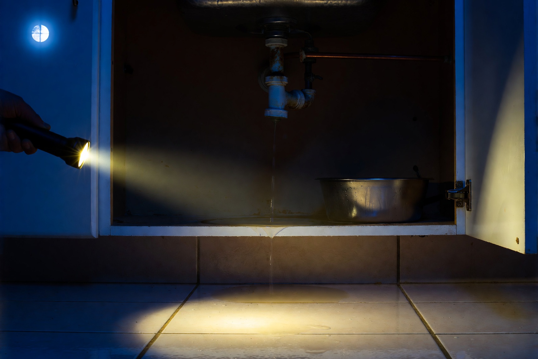 A flashlight on a leaking kitchen pipe at night.