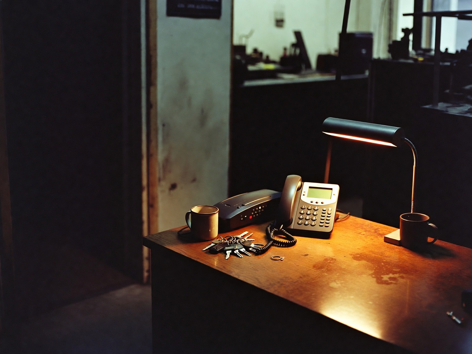 An empty trade shop office after close — desk lamp, landline, truck keys.